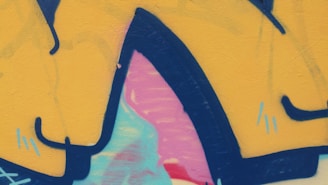 Brightly colored graffiti art featuring abstract shapes with bold outlines. The design includes shades of yellow, pink, blue, and red with black accents.