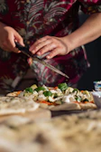 A chef sprinkling fresh herbs over a just-baked Indian fusion pizza in a warm kitchen.