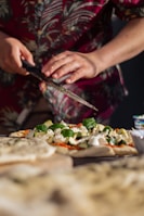 A chef sprinkling fresh herbs over a hot pizza in a cozy, white-themed pizzeria kitchen.