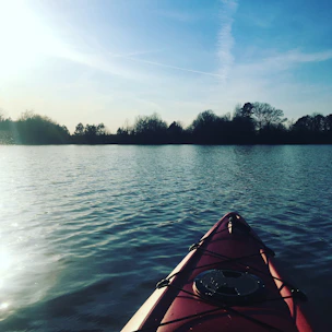 A bright red kayak resting on the sandy shore of a peaceful coastal inlet at sunrise.