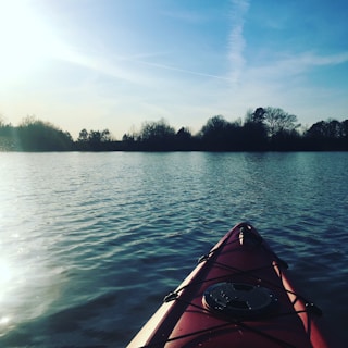 A bright red kayak resting on the calm water near a wooden dock at sunrise.