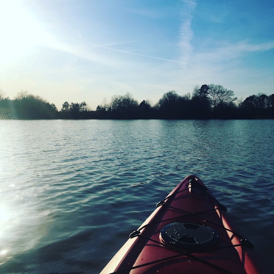 A bright red kayak resting on the calm water near a wooden dock at sunrise.