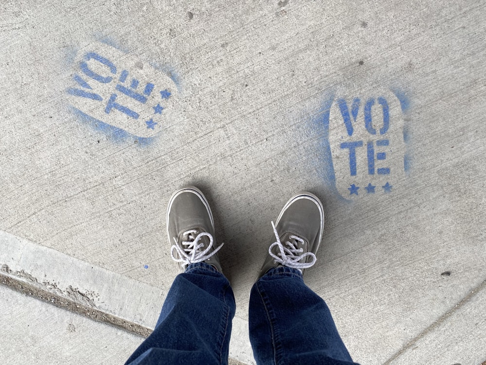 Persona con jeans de mezclilla azules y zapatillas blancas de pie sobre piso de concreto gris