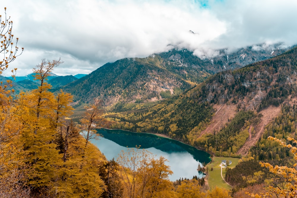 Montagnes vertes et brunes près du lac sous des nuages blancs pendant la journée