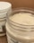 Two jars of cream or lotion with one open jar showing a smooth, creamy substance inside. The jars have white lids and label designs featuring text and botanical illustrations.