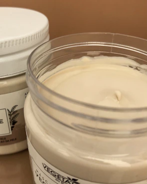 A hand holding a small jar of cream with a soft, creamy texture visible inside.