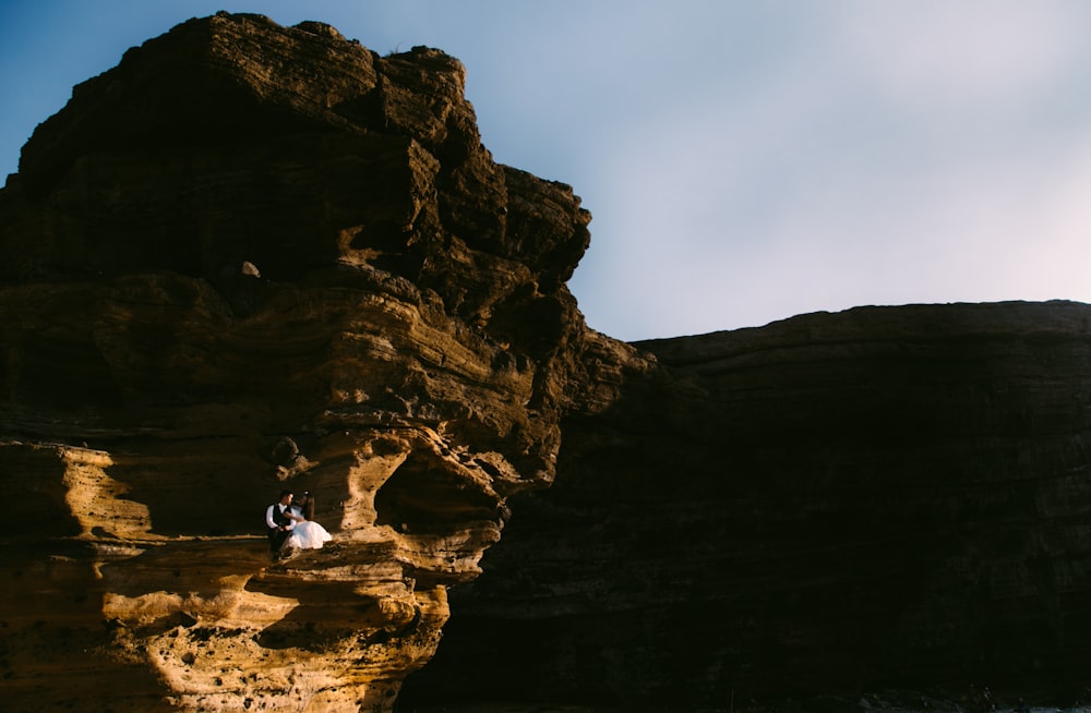 man in white shirt sitting on rock formation during daytime