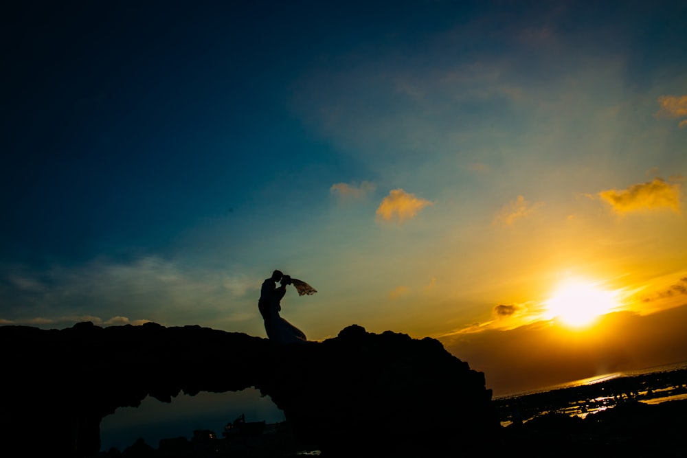 silhouette of person standing on rock formation during sunset