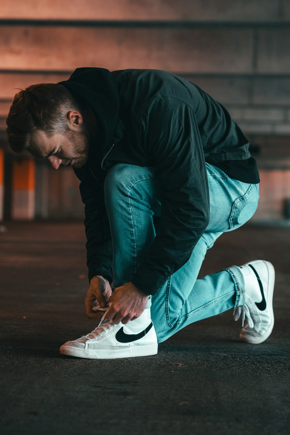 man in black jacket and blue denim jeans sitting on floor