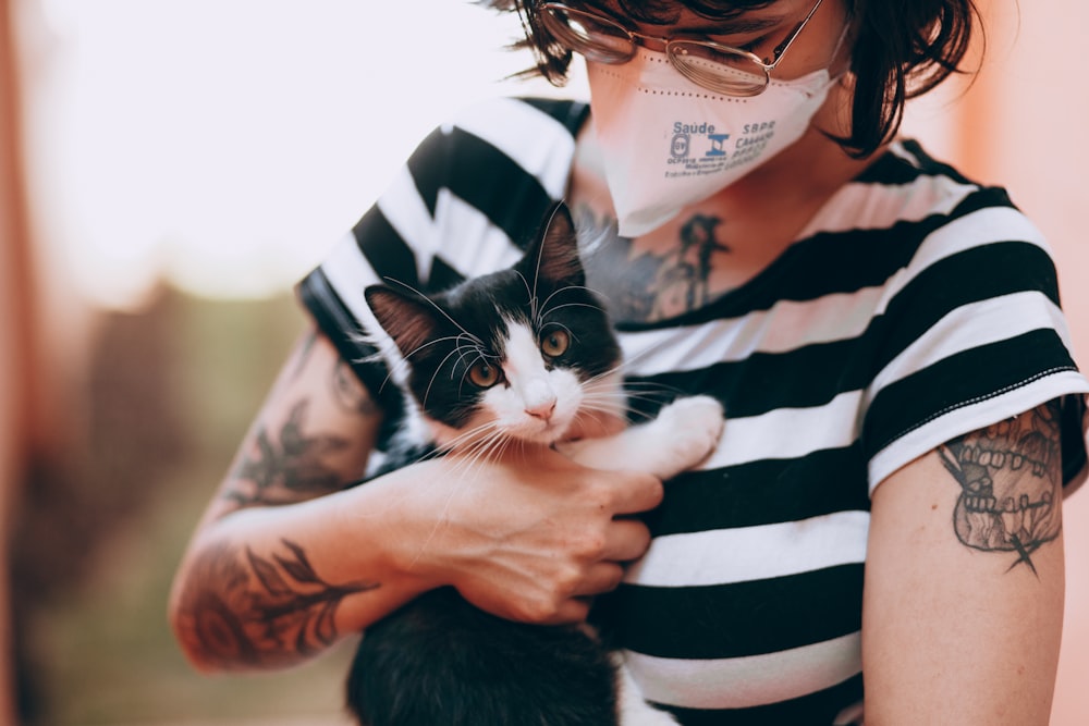 woman in black and white striped long sleeve shirt holding black and white cat