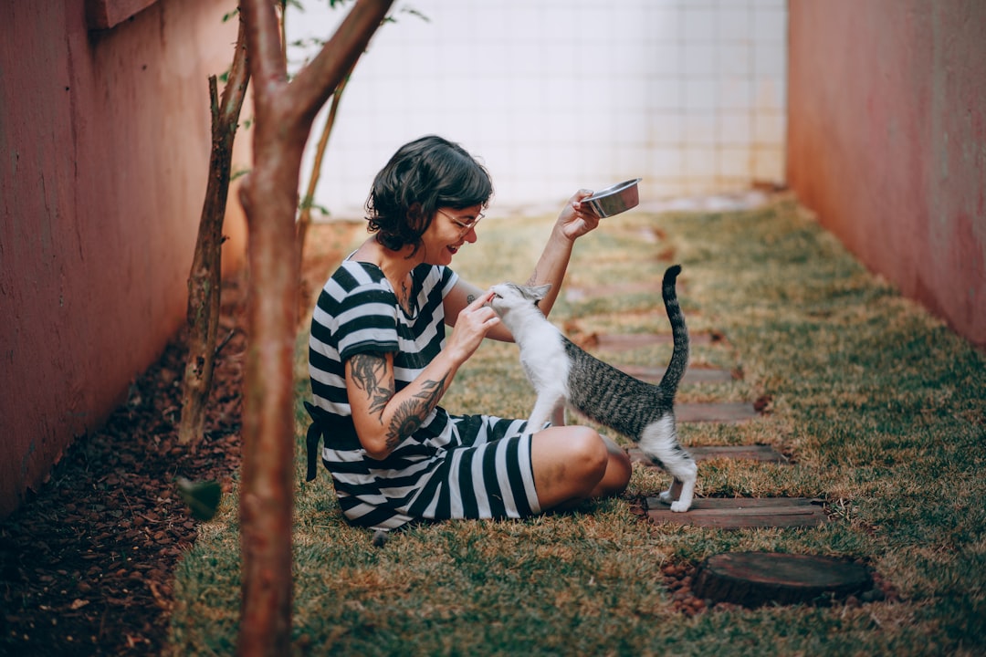 woman in black and white stripe long sleeve shirt sitting on ground with white cat