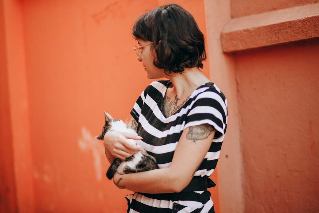 woman in black and white striped shirt carrying white and black cat