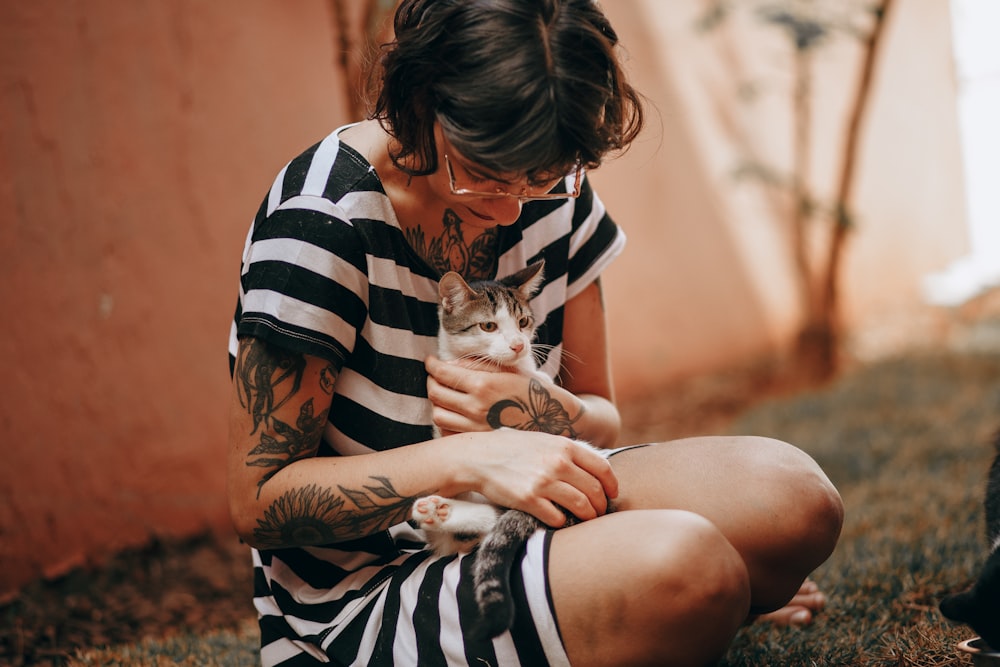 woman in black and white stripe shirt hugging white and black cat