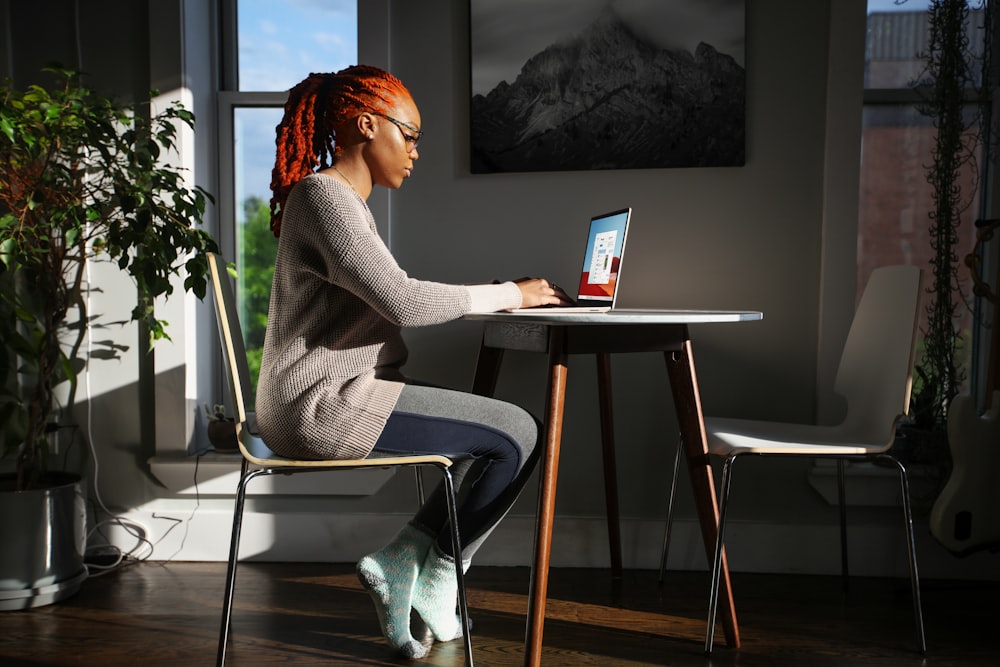 ノートパソコンを使って椅子に座っている灰色のセーターを着た女性