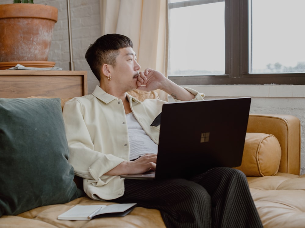 man in white dress shirt and black pants sitting on couch using Surface laptop