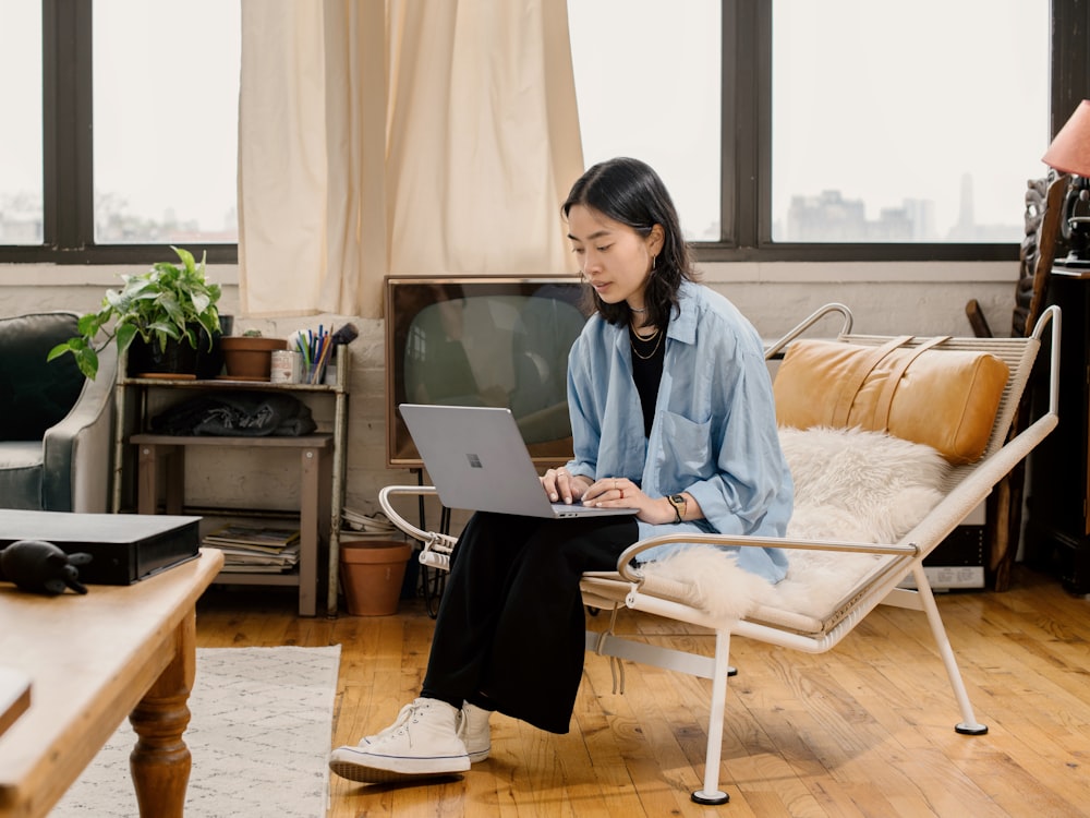 woman in blue shirt sitting on white chair using Surface laptop