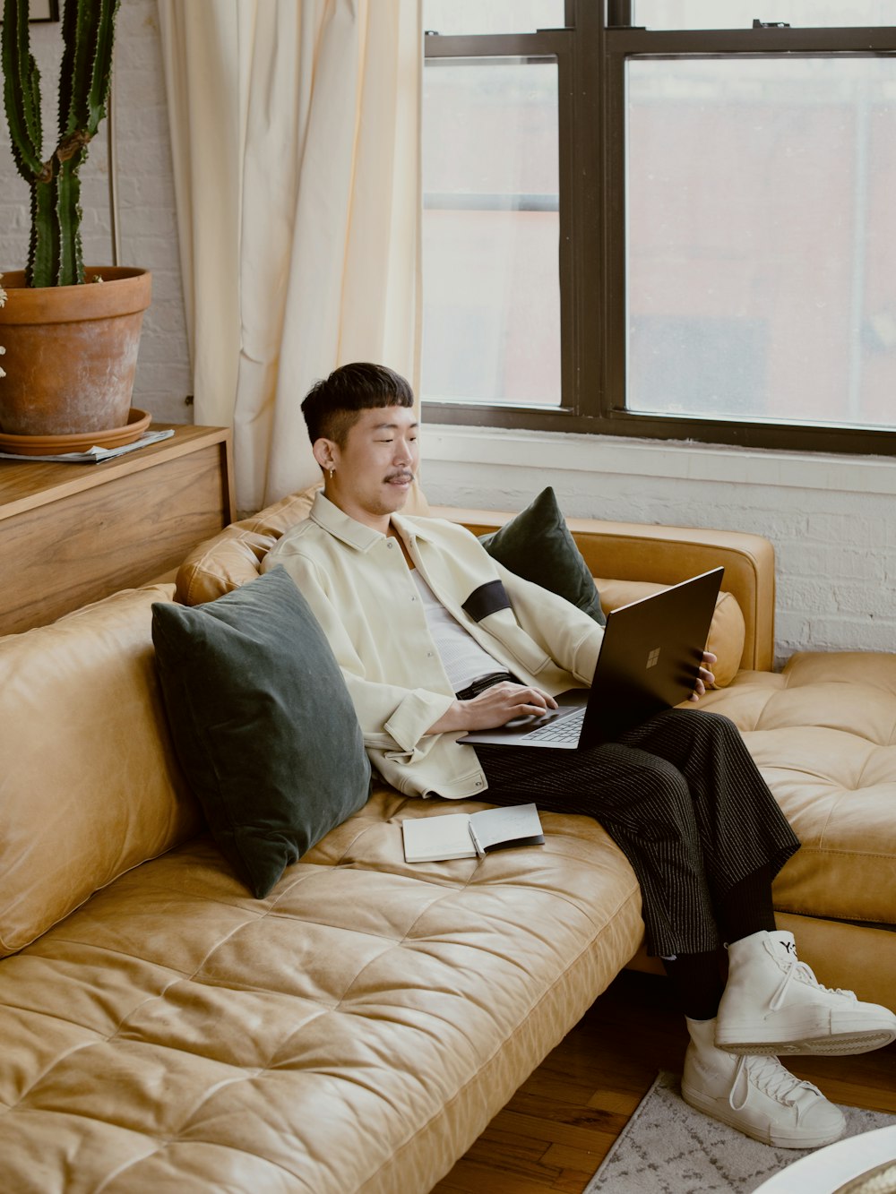 흰색 드레스 셔츠를 입은 남자가 검은색 Surface 노트북을 사용하여 흰색 소파에 앉아 있다