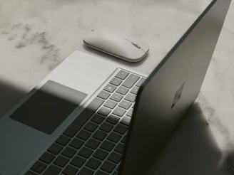 Microsoft Surface Laptop 4 open on a wooden desk next to a wireless Microsoft mouse.