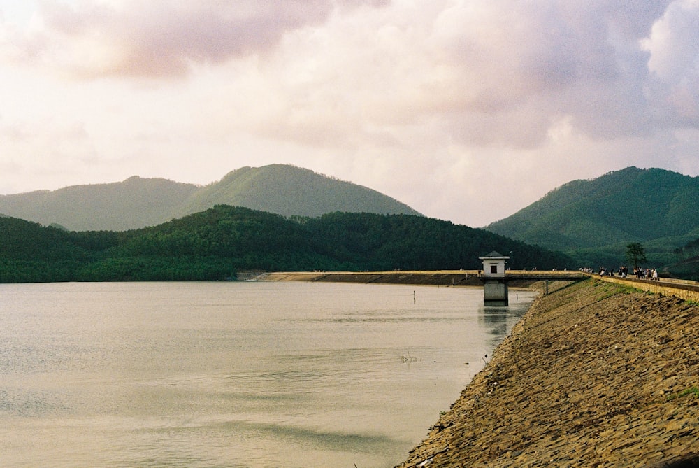 body of water near green mountain under white clouds during daytime