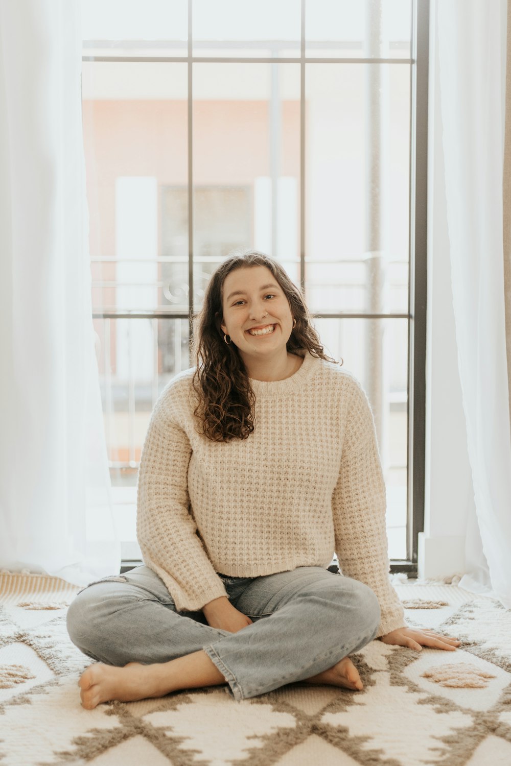 woman in pink sweater and blue denim jeans sitting on bed