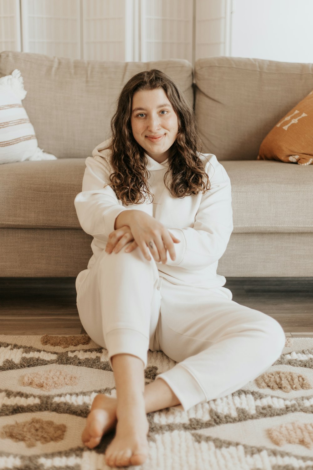 woman in white long sleeve shirt and white pants sitting on brown and black floral area