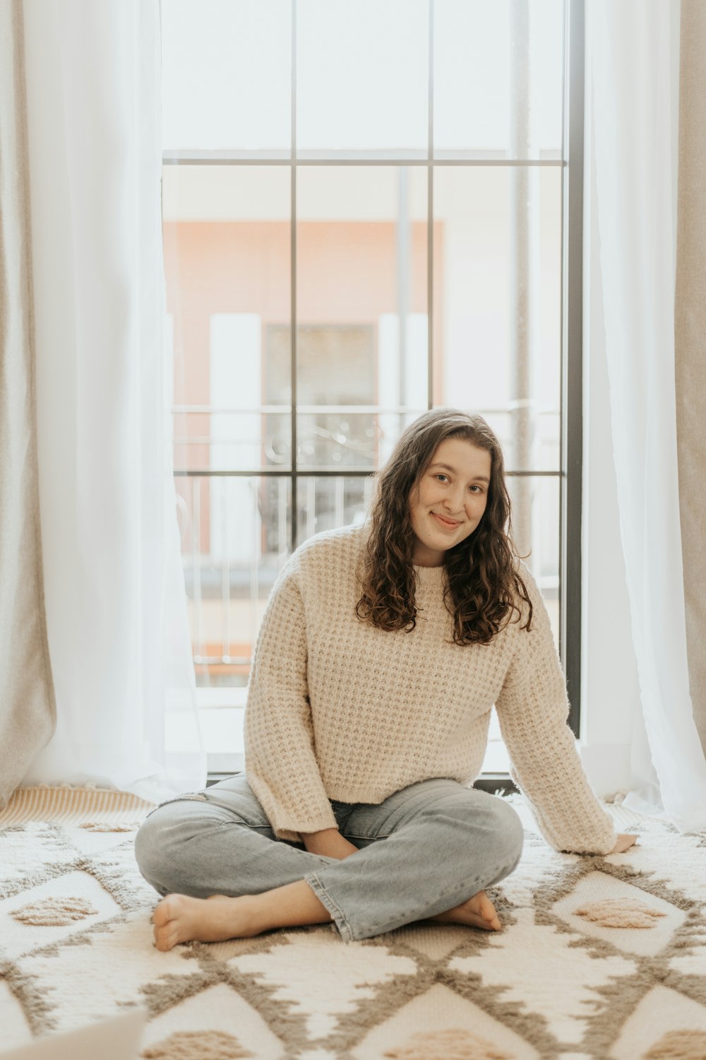 woman in white sweater and gray pants sitting on bed