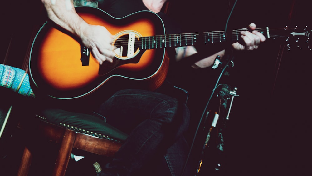 uomo in canottiera nera che suona la chitarra acustica