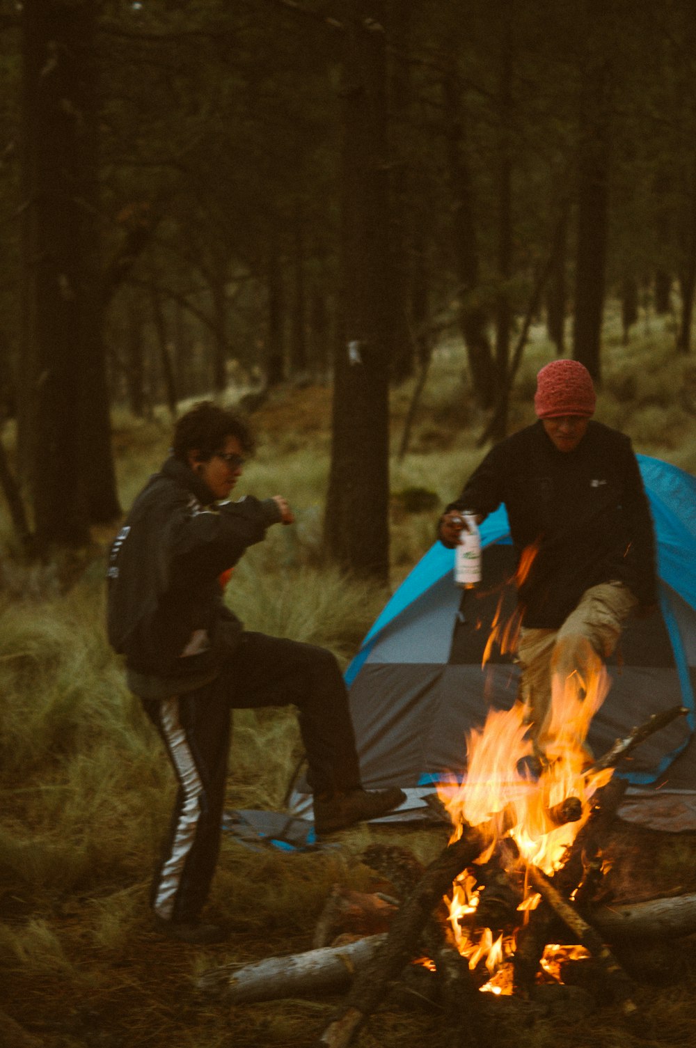 man in black jacket and black pants sitting on blue camping tent near bonfire during daytime