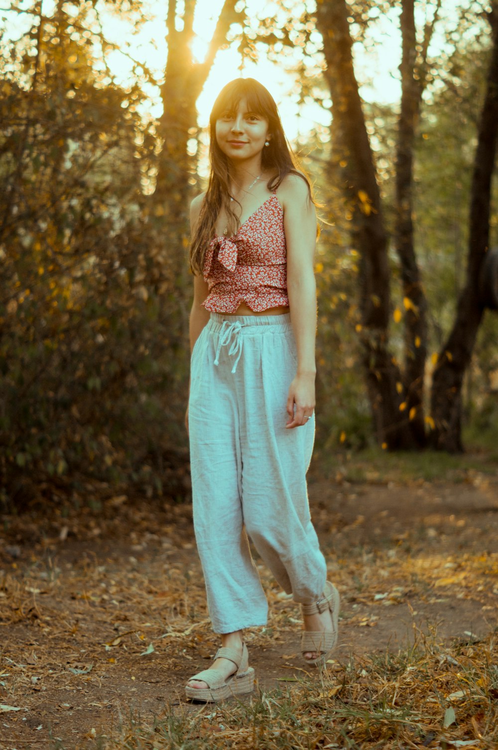 woman in pink and white floral tank top and white pants standing on brown soil