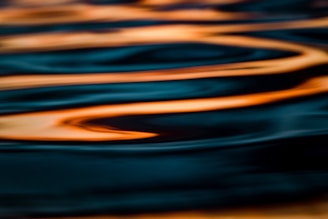 Close-up of hands creating ripples on a dark surface illuminated by violet and turquoise lights.