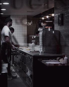 A cozy kitchen scene with a couple wearing chef hats, preparing gourmet pizza together with fresh Italian ingredients.