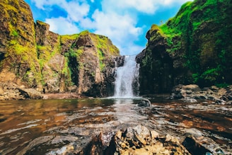 water falls on rocky mountain under blue sky during daytime