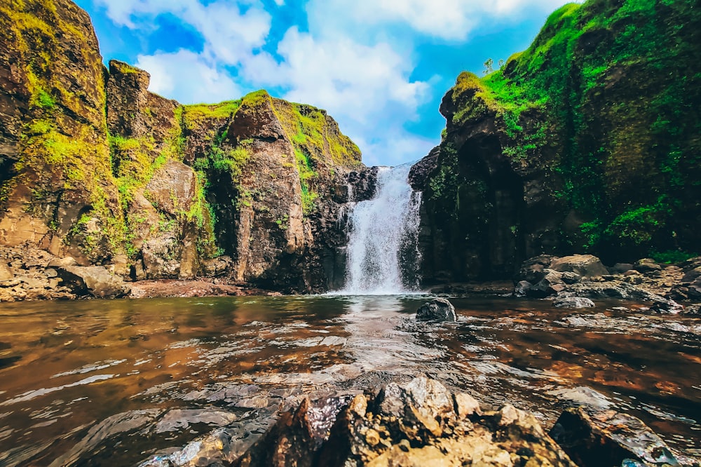 water falls on rocky mountain under blue sky during daytime