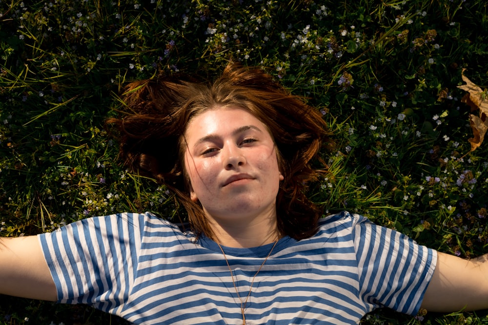 woman in white and blue striped shirt lying on green grass