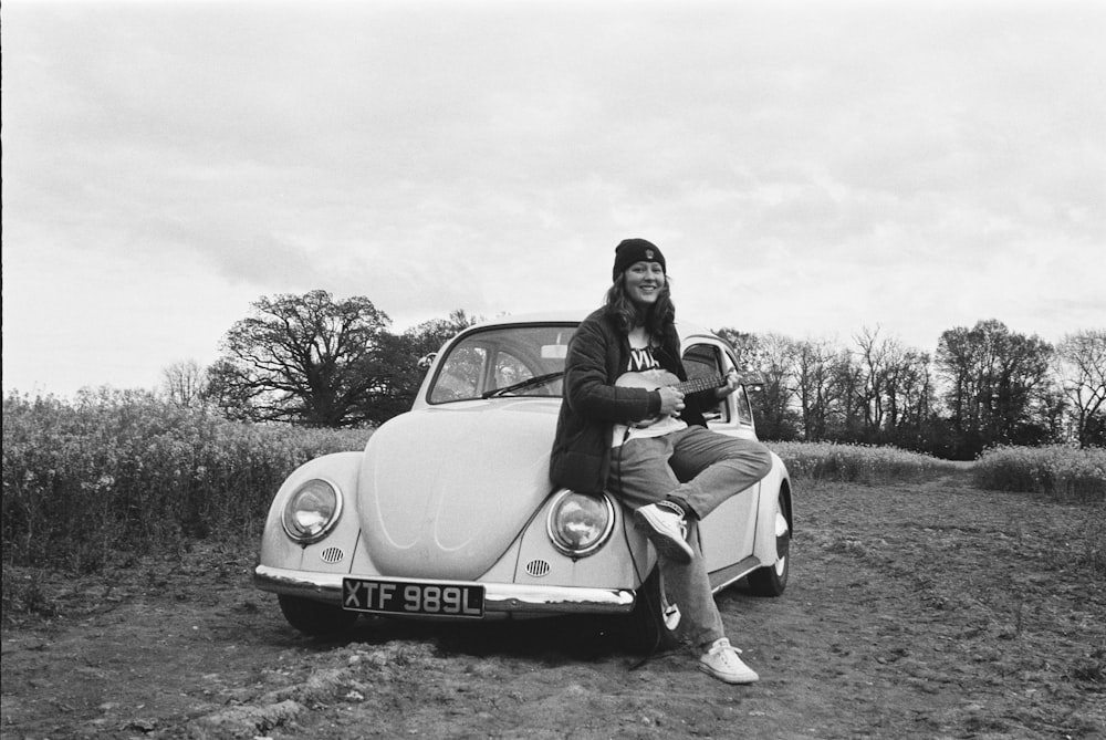 grayscale photo of man and woman sitting on car hood