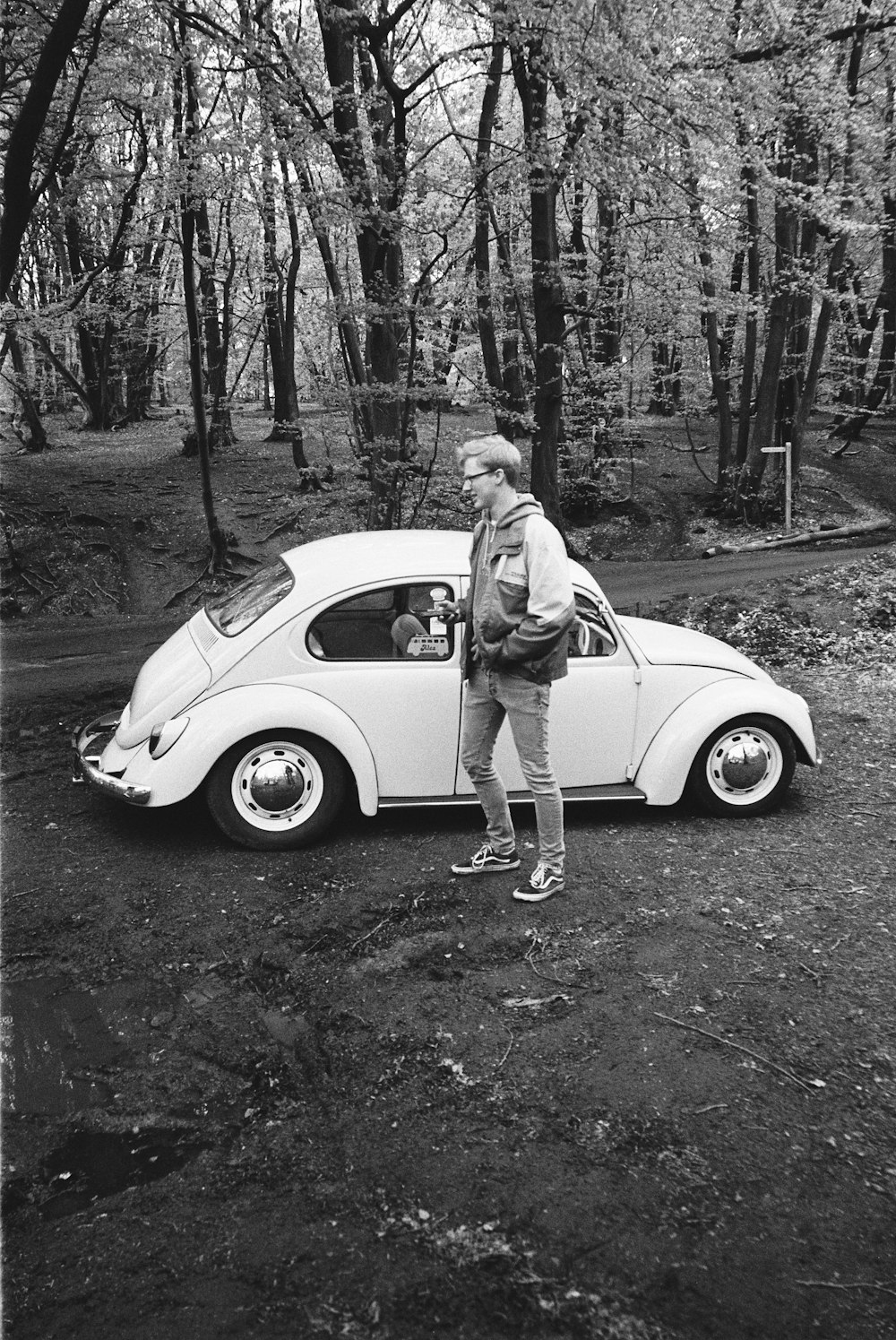 grayscale photo of woman in white dress standing beside white car