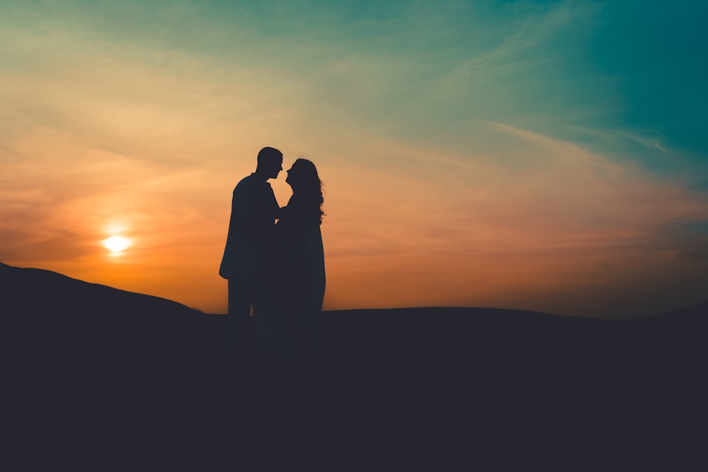 silhouette of couple standing on hill during sunset
