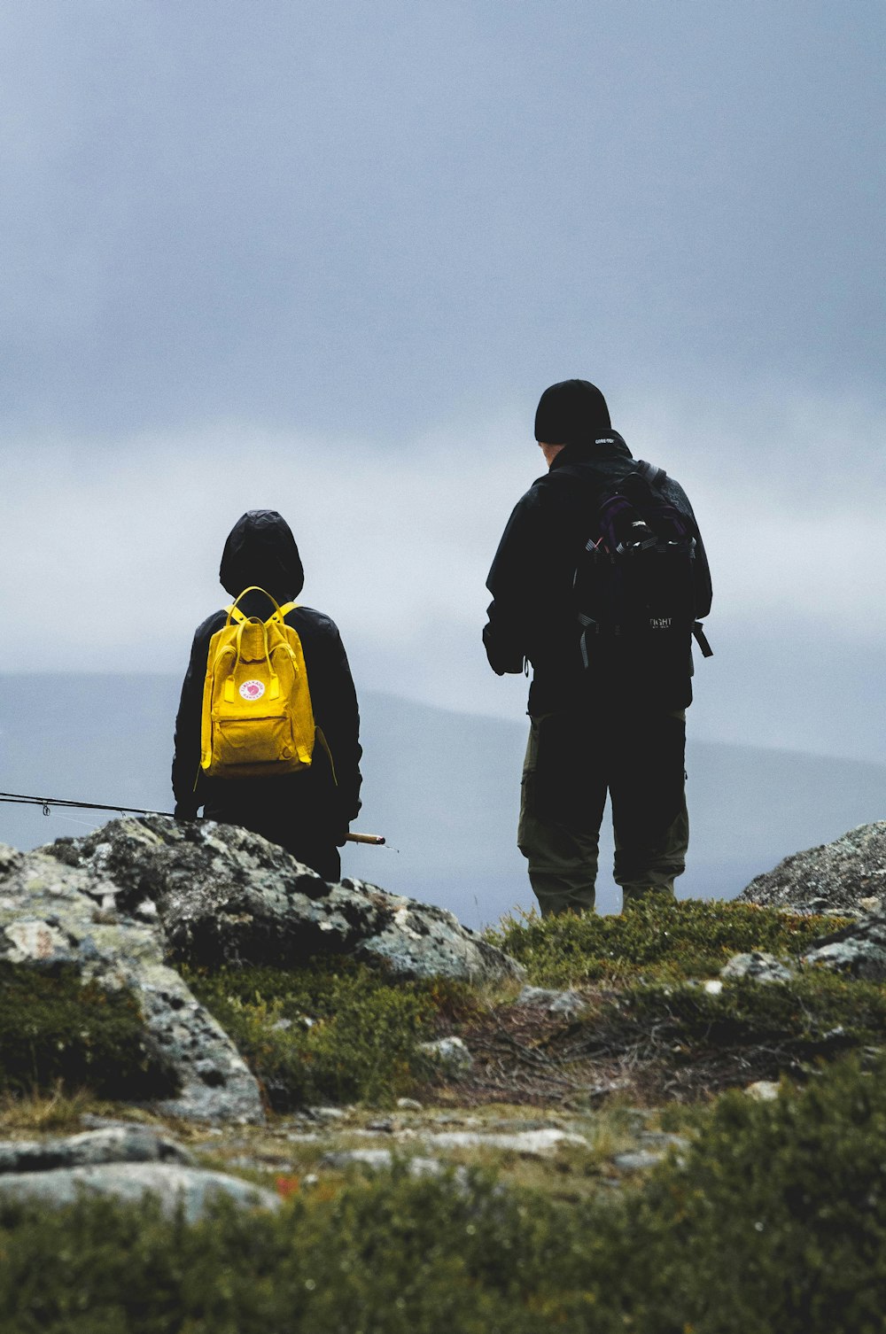 2 men in black and yellow backpacks standing on gray rock