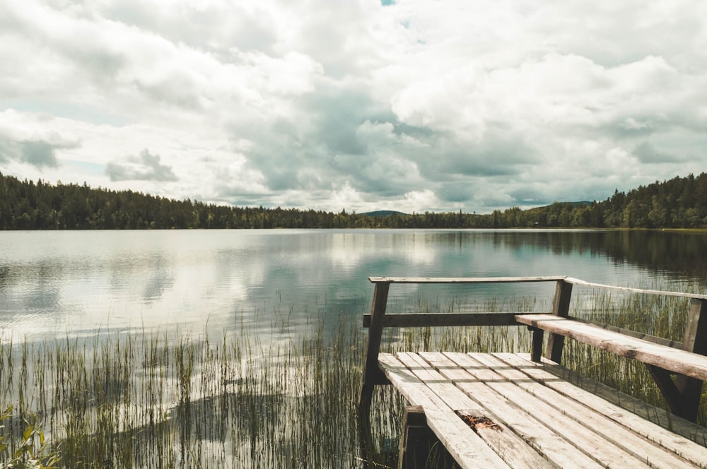 brown wooden dock on lake under white clouds during daytime