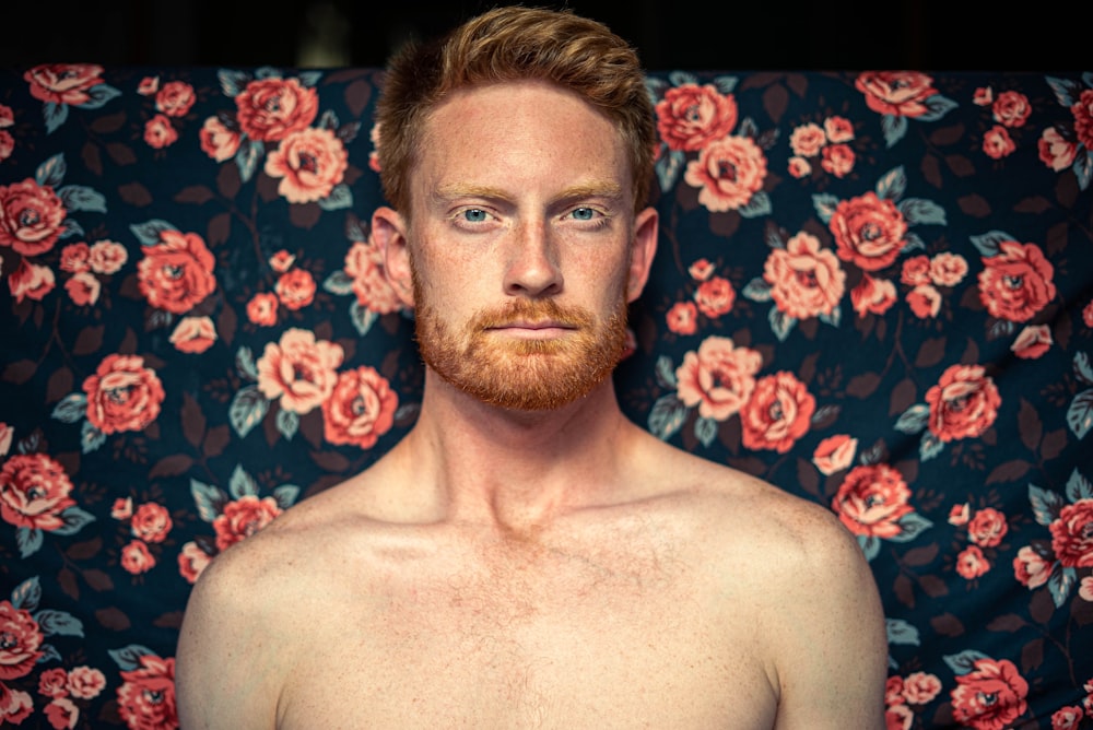 topless man sitting on purple and white floral textile