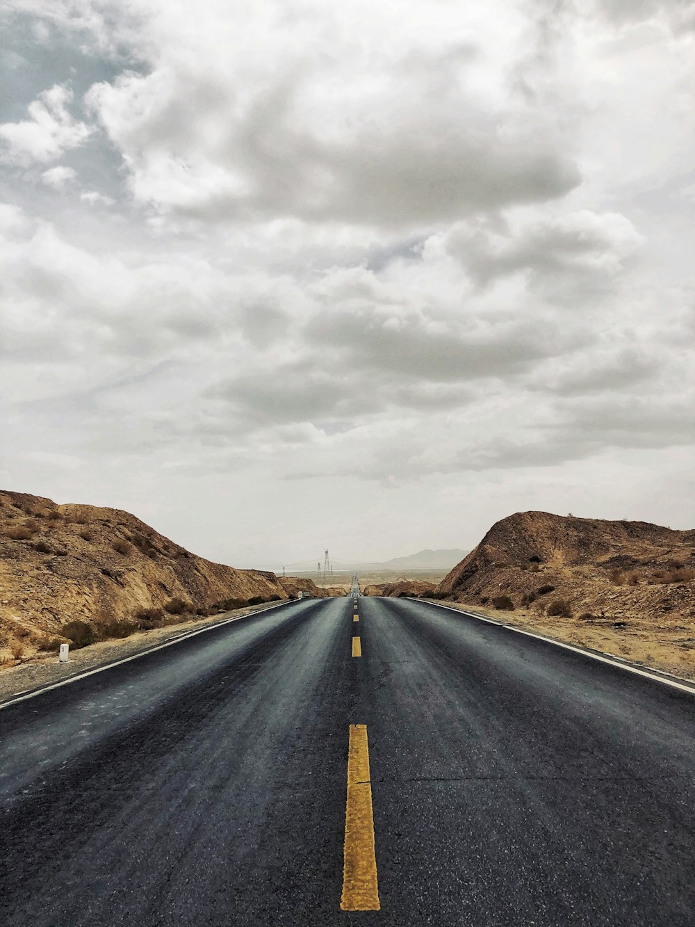 Carretera de asfalto negro entre montañas marrones bajo cielo nublado blanco durante el día