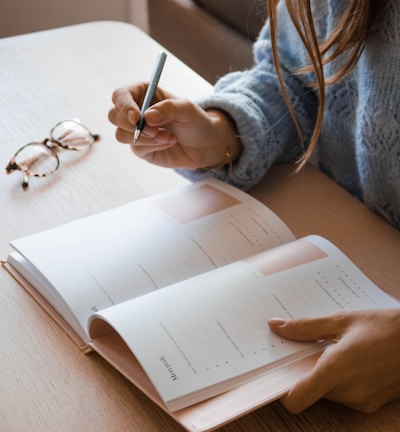 woman in white long sleeve shirt holding pen writing on white paper