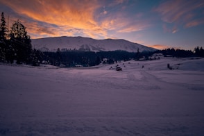 snow covered field near mountain under cloudy sky during daytime