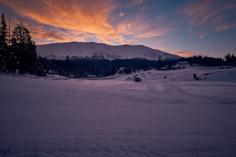 snow covered field near mountain under cloudy sky during daytime