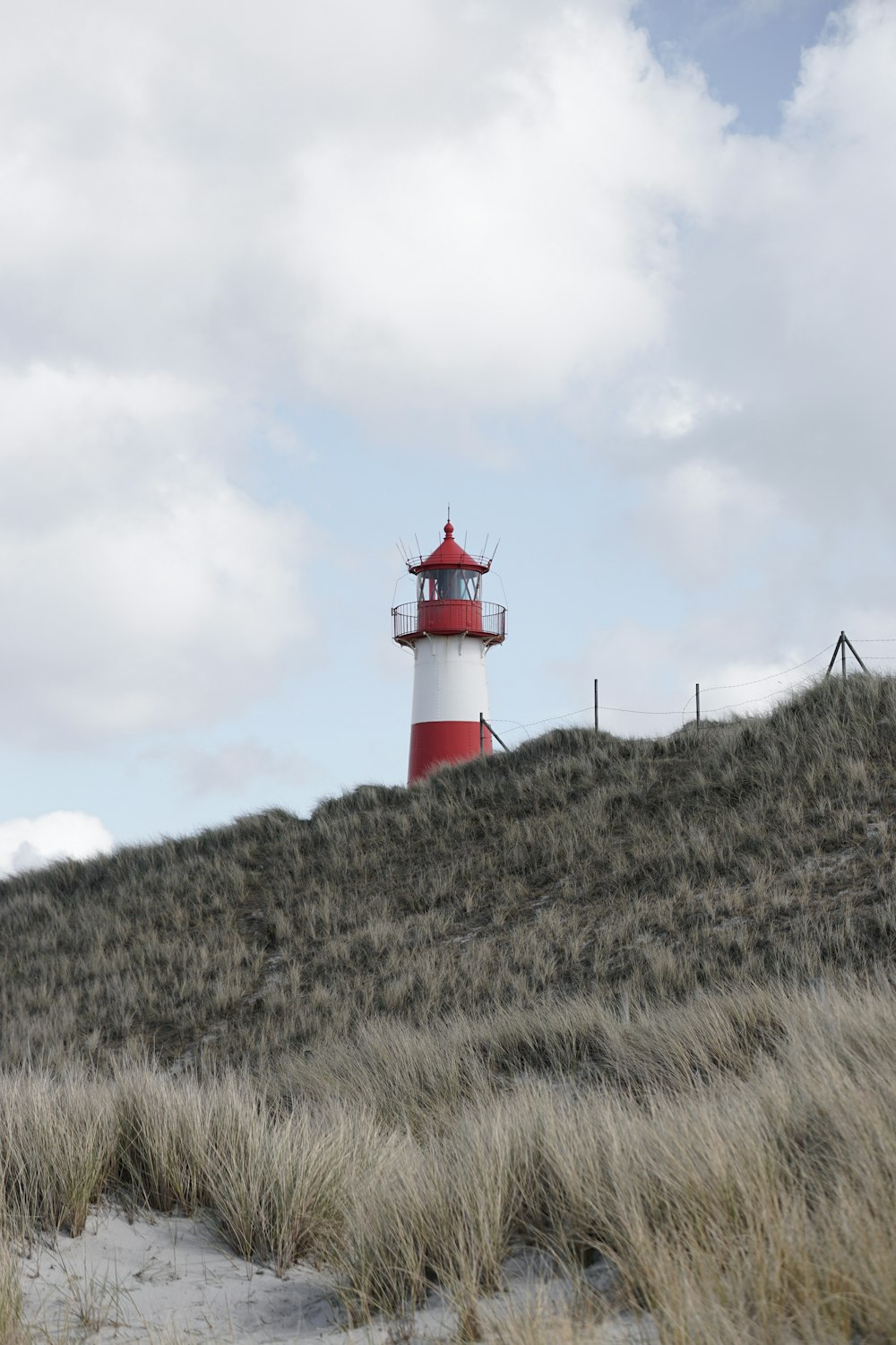 Rot-weißer Leuchtturm auf grünem Grasfeld unter weißen Wolken tagsüber