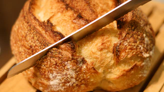 Close-up of a crusty, golden-brown bread loaf being sliced with a serrated knife.