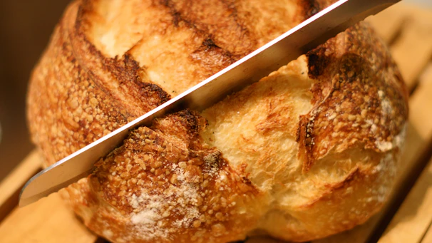 Close-up of a crusty, golden-brown bread loaf being sliced with a serrated knife.