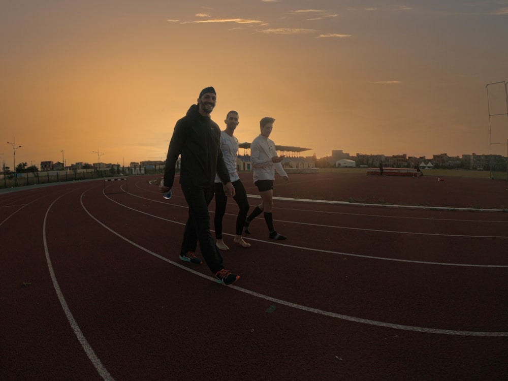 man in black jacket and black pants walking on track field during sunset