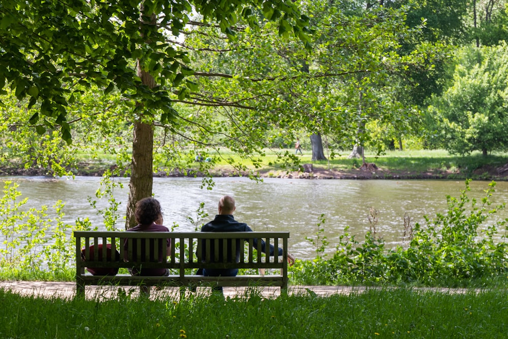 2 women sitting on bench near body of water during daytime