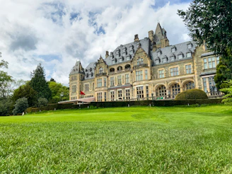 A majestic historic mansion with intricate stonework and a beautifully landscaped front yard.
